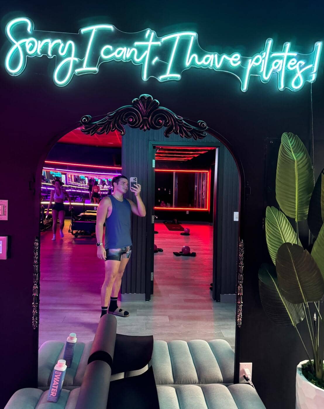 Member taking a mirror selfie under the Sorry I can't, I have pilates neon sign at HILI Fitness Lake Nona pilates studio