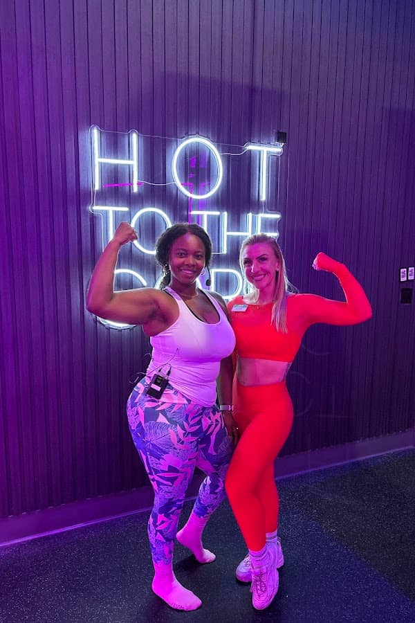Two members flexing under the Hot to the Core neon sign in the HILI Lake Nona infrared hot mat room