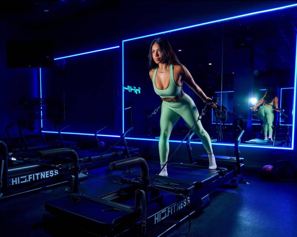 Member balancing on an XFormer pilates machine in the blue-lit strength room at HILI Fitness